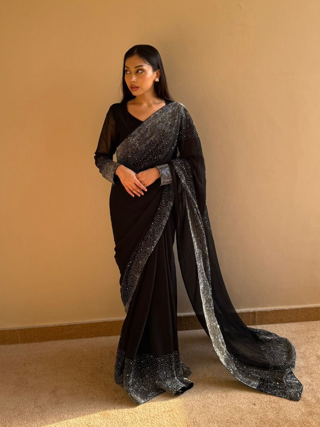 Woman wearing a black saree with silver border against a beige wall.